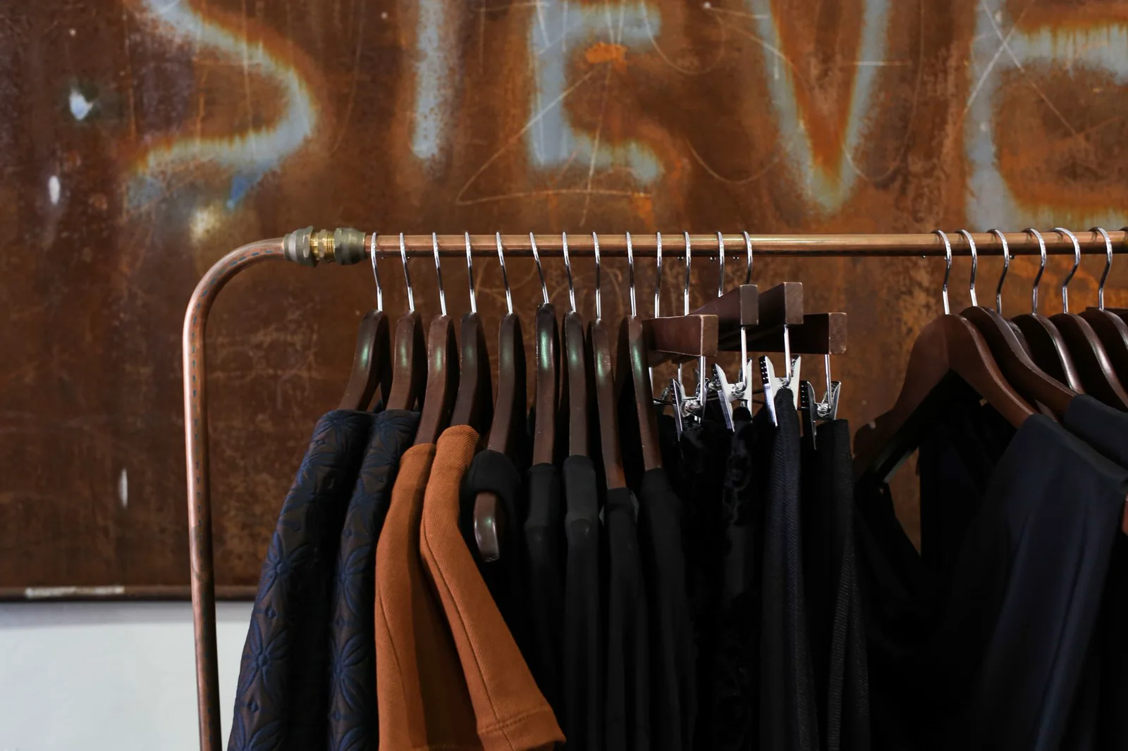 Conceptual close view of dark garments on a copper clothing rack